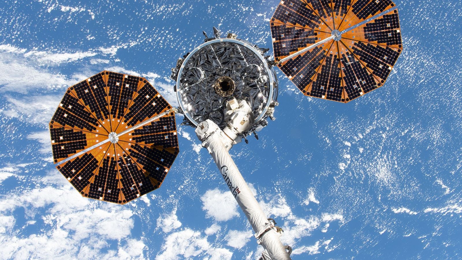 Грузовой космический корабль Cygnus XL компании Northrop Grumman в захвате манипулятора Canadarm2 над Землёй, с двумя раскрытыми круглыми солнечными батареями